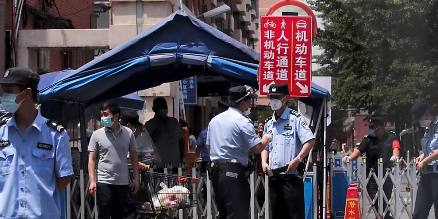 Polizeibeamte und Sicherheitsbeamte, die Schutzmasken tragen, stehen vor Wohngebäuden Wache, die nach einem positiven Fall auf einem nahe gelegenen Markt abgeriegelt wurden. Foto: Andy Wong/AP/dpa