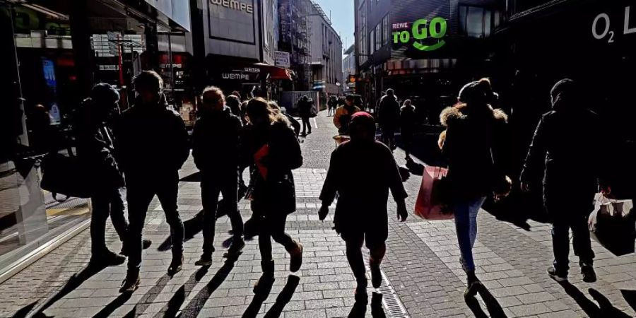 Passanten werfen in einer Kölner Fussgängerzone lange Schatten. Foto: Oliver Berg/dpa