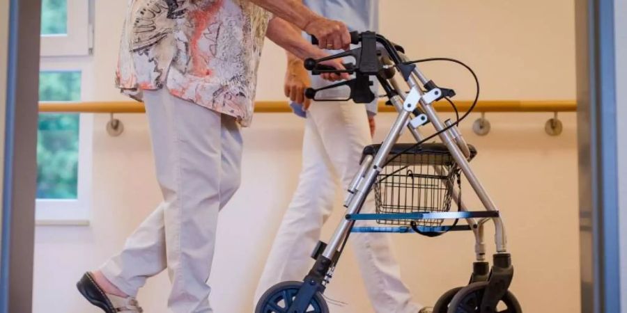 Eine Pflegekraft geht mit einer älteren Frau über einen Korridor in einem Pflegeheim. Der Mindestlohn für mehr als eine Million Pflegekräfte in Deutschland wird erhöht. Foto: Christoph Schmidt/dpa