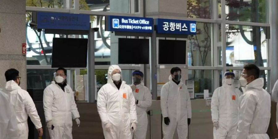 Quarantäne-Beauftragte in Schutzkleidung warten in der Ankunftshalle des internationalen Flughafens Incheon auf Reisende, um sie zu ihren Quarantäne-Unterkünften zu führen. Foto: Ahn Young-Joon/AP/dpa
