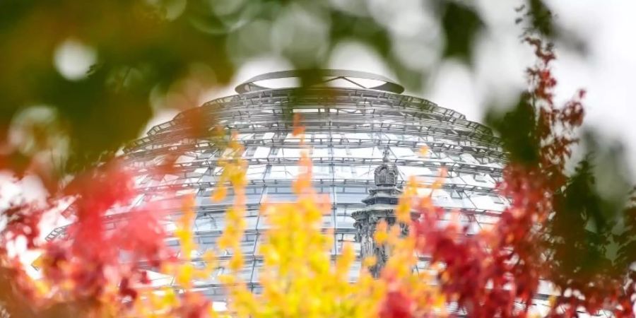 Rot-gelb-grün herbstlich verfärbte Blätter sind an Bäumen vor der Reichstagskuppel zu sehen. Foto: Britta Pedersen/dpa-Zentralbild/dpa