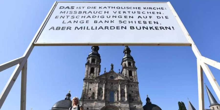 Ein Plakat der Giordano-Bruno-Stiftung mit der Aufschrift "DAS ist die Katholische Kirche: Missbrauch vertuschen. Entschädigungen auf die lange Bank schieben. Aber Milliarden bunkern !" steht am Rande der Herbstvollversammlung der Deutschen Bischofskonferenz auf dem Platz vor dem Dom. Foto: Arne Dedert/dpa