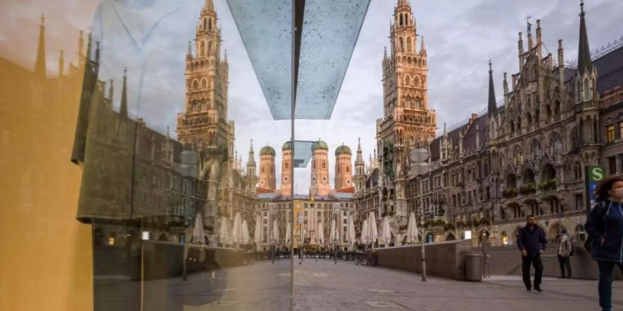 Passanten gehen über den Marienplatz in der Münchner Innenstadt. Hintergrund sind die Zwillingstürmen der Frauenkirche (l) und das Neue Rathaus (r) zu sehen. Foto: Peter Kneffel/dpa