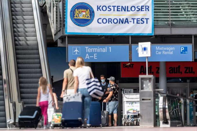 Reisende gehen am Flughafen in Richtung eines Banners mit der Aufschrift «Kostenloser Corona-Test». Für alle Fluggäste werden am Flughafen kostenlose Corona-Tests angeboten. Foto: Matthias Balk Test Bayern Corona