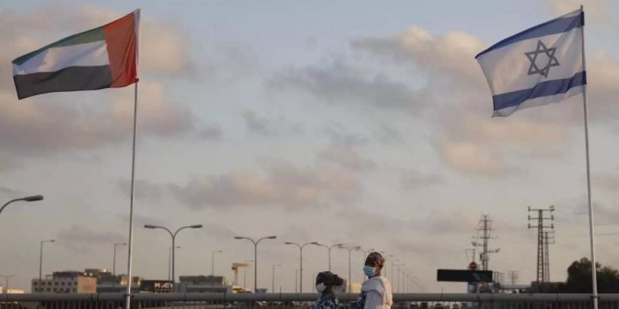 Frauen mit Schutzmasken gehen an den Flaggen von Israel und den Vereinigten Arabischen Emiraten auf der Friedensbrücke im israelischen Netanya vorbei. Foto: Ariel Schalit/AP/dpa
