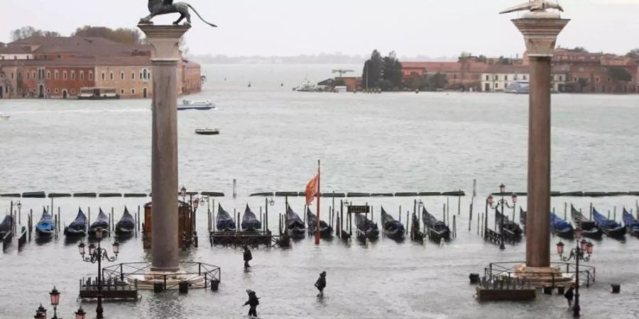 Menschen gehen knietief in Wasser über den überfluteten Markusplatz. Foto: Luca Bruno/AP/dpa