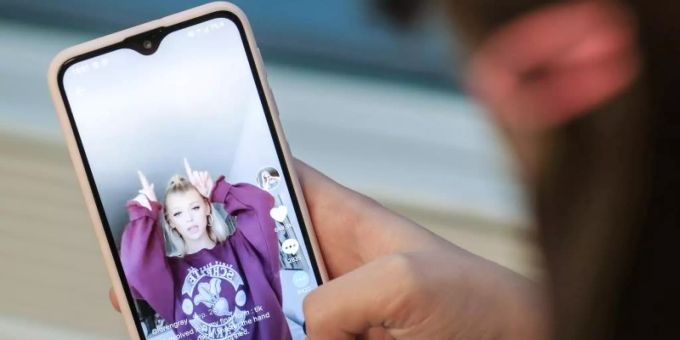 Ein Mädchen hält ihr Smartphone in den Händen, auf dem sie in der Kurzvideo-App TikTok das Profil von @lorengray geöffnet hat. Foto: Jens Kalaene/dpa-Zentralbild/dpa teenager