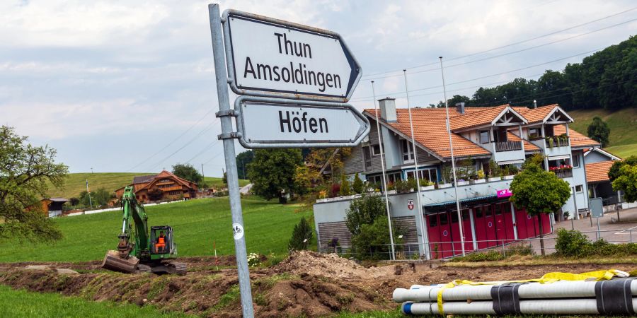 Ein Strassenwegweiser in Richtung Thun, Amsoldingen, Höfen sowie eine Baustelle in Oberstocken. Hinten das Gebäude, in welchem das Feuerwehrmagazin und die Gemeindeverwaltung Stocken-Hofen untergebracht sind.