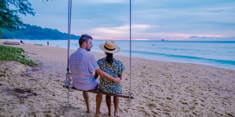 Pärchen auf einer Schaukel im Sonnenuntergang am Strand.