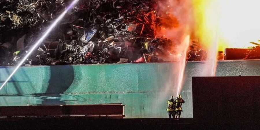 Ein grosser Schrotthaufen brennt und wird von Feuerwehrleuten gelöscht. Foto: Kohls/SDMG/dpa