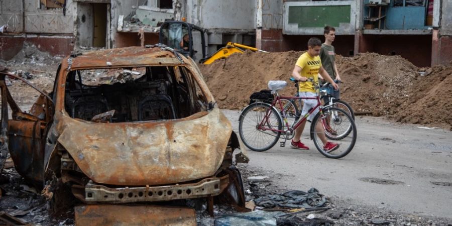 Zwei Jungen schieben ihre Fahrräder an zerstörten Autos und Wohngebäuden in Tschernihiw vorbei. Foto: Michal Burza/ZUMA Press Wire/dpa