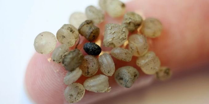 Mikroplastik-Teilchen kleben an einem Klebestreifen an einem Finger. Mikroplastik-Teilchen kleben an einem Klebestreifen an einem Finger.