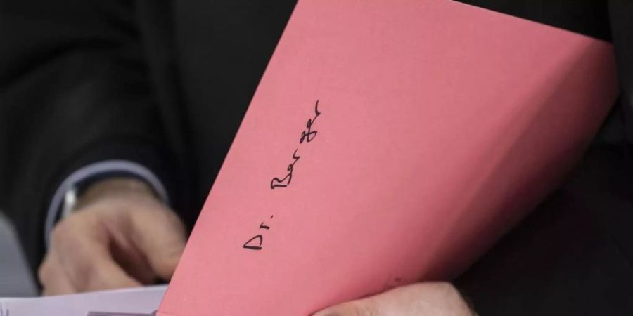 Ein Rechtsanwalt des Hauptbeschuldigten Hanno Berger mit eine Akte mit der Aufschrift «Dr. Berger». Foto: Boris Roessler/dpa/Archiv