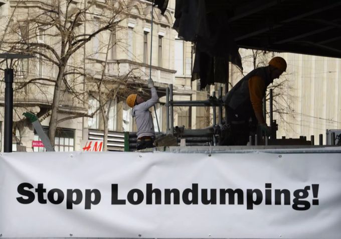 Ein Banner mit dem Schriftzug «Stopp Lohndumping» hängt an der Fassade des ehemaligen «Bally-Hauses» und zukünftigen Geschäftes des Modelabels «Zara» an der Zürcher Bahnhofstrasse, am 25. Februar 2014. Die Gewerkschaft Unia hatte die Arbeiten im «Bally-Haus» zum Erliegen gebracht. Damit wollte sie gegen die Dumpinglöhne vorgehen, welche den Bauarbeitern aus Spanien bezahlt wurden. Im Bild sind Schweizer Bauarbeiter mit dem Abbau des Gerüstes beschäftigt. Flankierende Massnahmen Rahmenabkommen