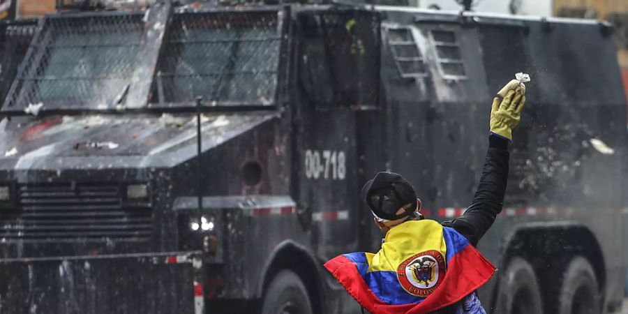 Ein wirft in einem Aussenbezirk von Bogotá einen Farbbeutel auf ein Polizeifahrzeug. Foto: Ivan Valencia/AP/dpa