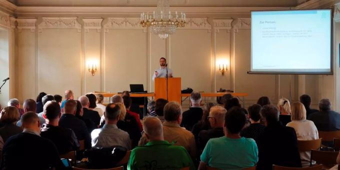 Hans-Ruedi Hottiger erläutert die anstehenden Arbeiten zum Agglomerationsprogramm. Mann präsentiert am Podium vor einer Gruppe Menschen