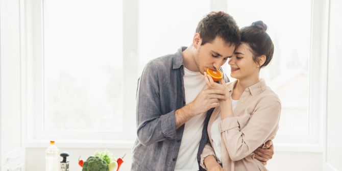 Junger Mann beisst in eine Orange, die seine Partnerin in der Hand hält