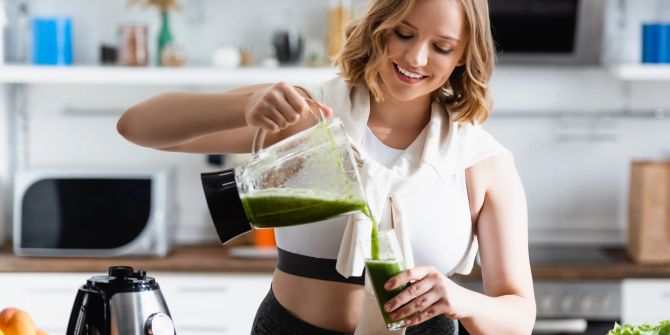 Lächelnde Frau bereitet grünen Smoothie zu