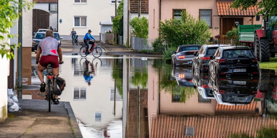 Radler fahren durch eine überflutete Strasse. Im Bereich der Gemeinde Baar-Ebenhausen war ein Damm an zwei Stellen geborsten.