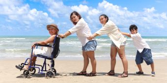 Familie mit Frau im Rollstruhl am Strand.