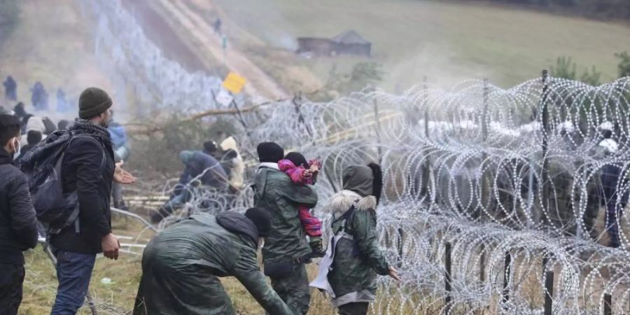 Migranten Anfang November an der belarussisch-polnischen Grenze. Hinter dem Stacheldrahtzaun steht die Polizei. Foto: Leonid Shcheglov/BelTA/AP/dpa