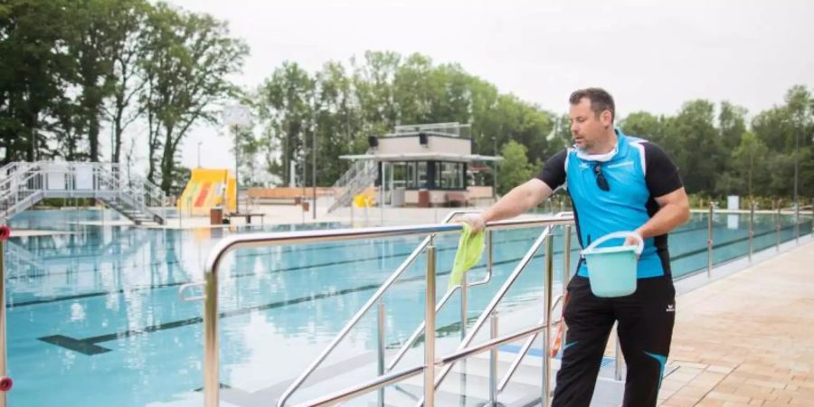 Neue Aufgaben: Der Schwimmmeister Björn Bendias in Ochtrup desinfiziert zwischen zwei Schwimmzeiten die Handläufe neben dem Schwimmbecken im Bergfreibad. Foto: Rolf Vennenbernd/dpa