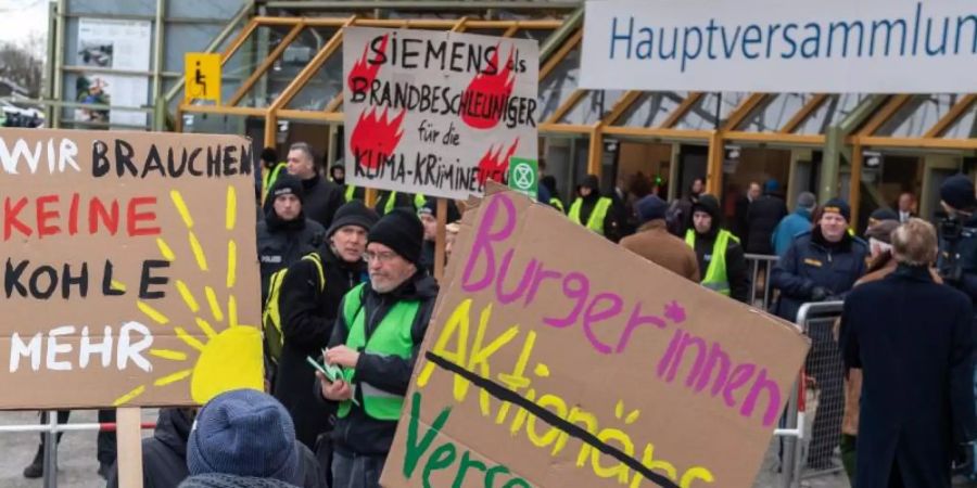 Klimaaktivisten demonstrieren mit Plakaten vor der Olympiahalle in München, wo die Siemens-Hauptversammlung stattfindet. Foto: Peter Kneffel/dpa