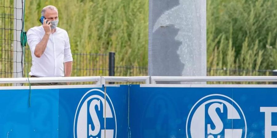 Schalkes Sportvorstand Jochen Schneider steht beim Training hinter einer Bande und telefoniert mit seinem Handy. Foto: Guido Kirchner/dpa/Archivbild