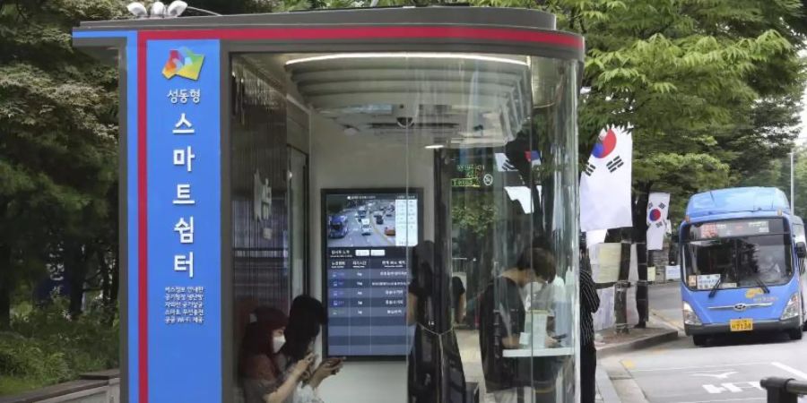 Menschen warten in Seoul in einem «smarten» Wartehäuschen auf den Bus. Foto: Ahn Young-Joon/AP/dpa