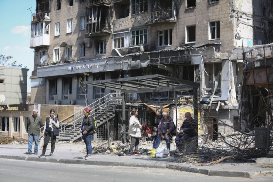 Einheimische stehen und sitzen am 17. Mai 2022 vor einem zerstörten Gebäude in Mariupol.