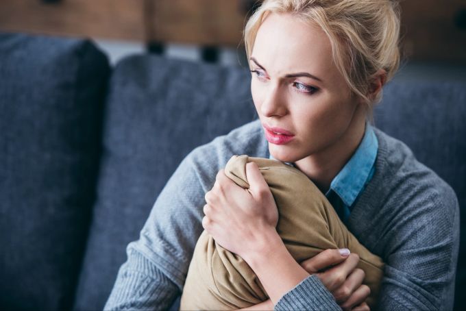 Sind Depressionen und Angsstörungen die neue Norm? Ängstliche und traurige Frau sitzt auf Couch und hält Kissen fest.