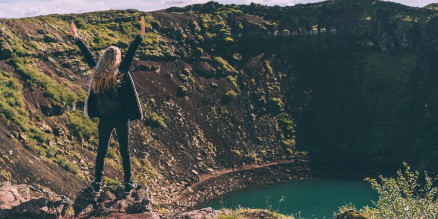 frau erhebt die arme, am steinbruch stehend, mit wasser gefüllt