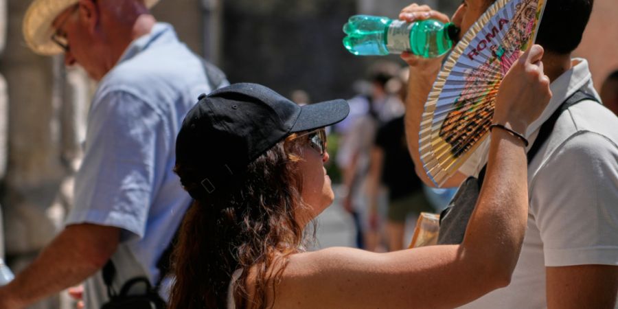 Eine Frau fächert sich Rom mit einem Fächer Luft zu, während ein Mann aus einer Wasserflasche trinkt. Foto: Gregorio Borgia/AP/dpa