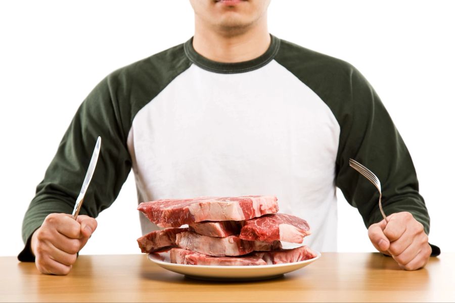 Viel Fleisch auf einem Teller und Mann mit Gabel und Messer.