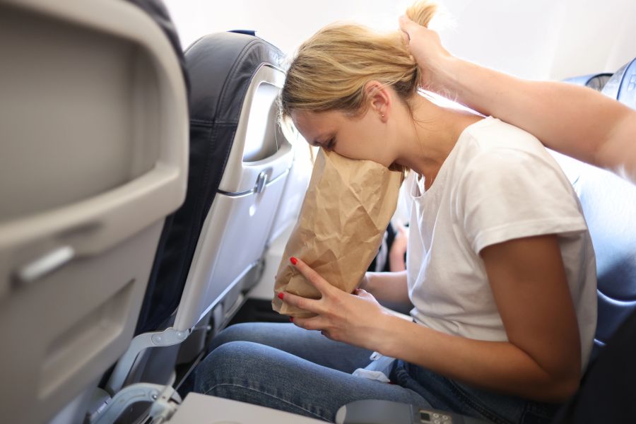 Frau im Flugzeug übergibt sich in eine Tüte