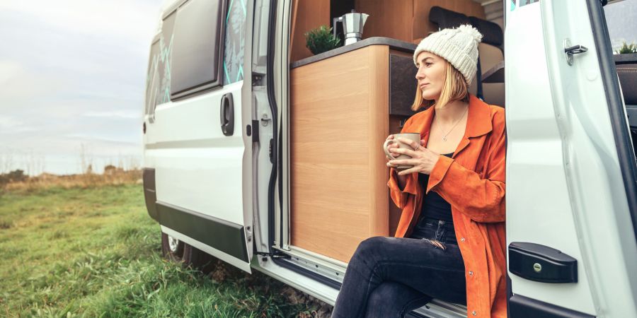 Frau sitz in der Tür eines Wohnmobils mit einer Tasse