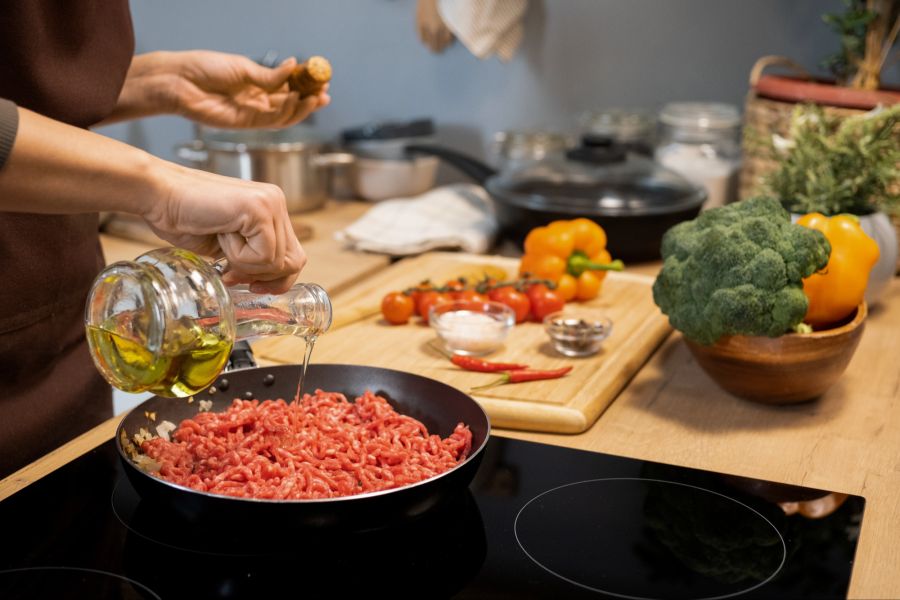 Person kipp Olivenöl in eine Pfanne mit Fleisch