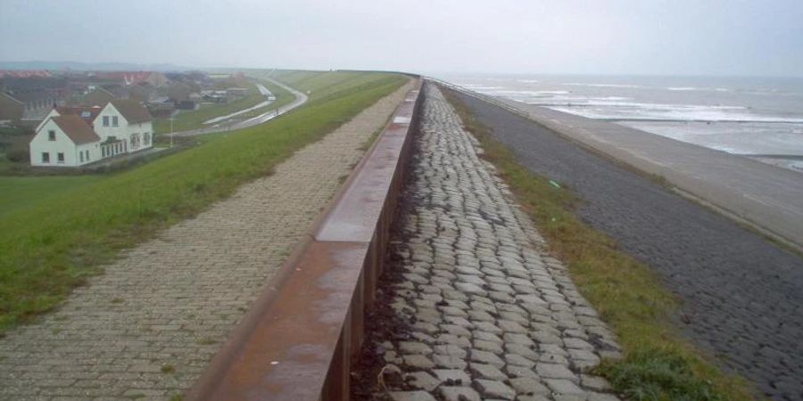 Ein Ort liegt an einem Deich hinter einem Strand in den Niederlanden. Foto: picture alliance / dpa