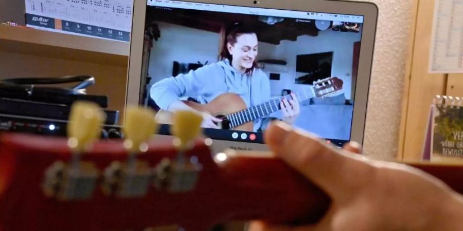 Ein Gitarrenlehrer unterrichtet eine Schülerin via Online-Videokonferenz. Foto: Peter Kneffel/dpa
