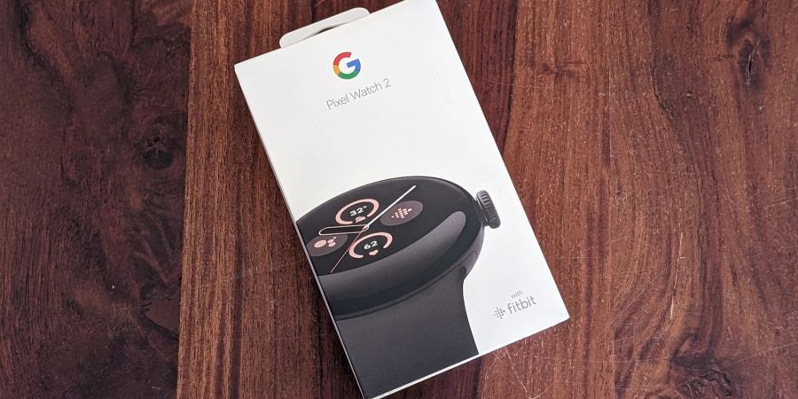 Eine Verpackung einer Pixel Watch 2 liegt auf einem Holztisch.