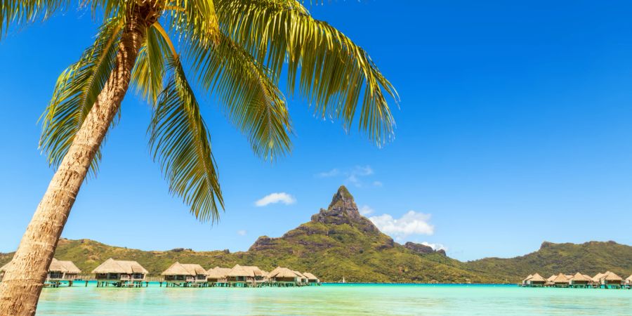 Berg ragt aus dem blauen Meer in Tahiti vor Wasserbungalows