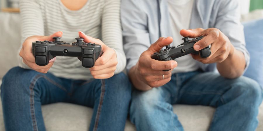 Ein Mann und eine Frau sitzen auf einer Couch und halten jeweils eine Spielekonsole in der Hand.