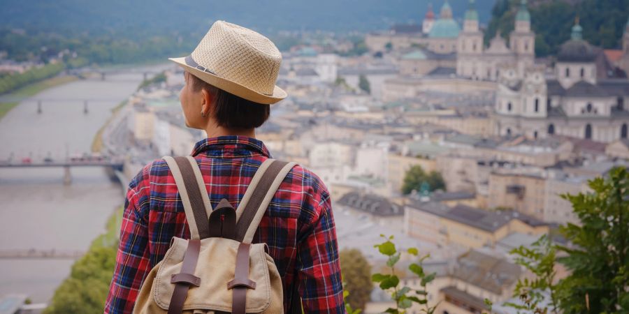 Frau von hinten mit Reiserucksack. Blick auf Stadt am Fluss.