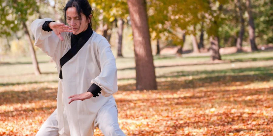 Frau macht im Wald Tai-Chi-Übungen im weissen Anzug.