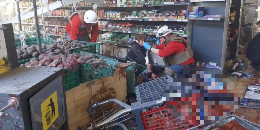 Eine Frau sitzt nach einem Bomben-Anschlag in einem Supermarkt – neben ihr liegt ein Toter.