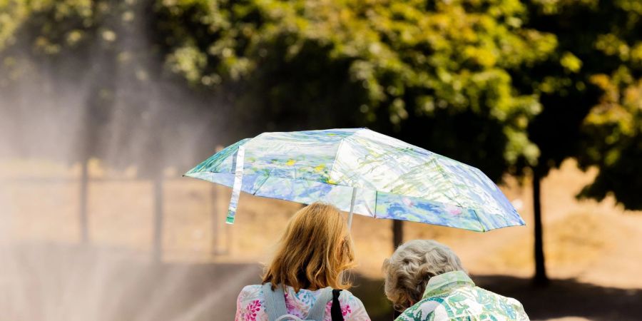 Zwei Frauen schützen mit einem Regenschirm vor der Sonne.