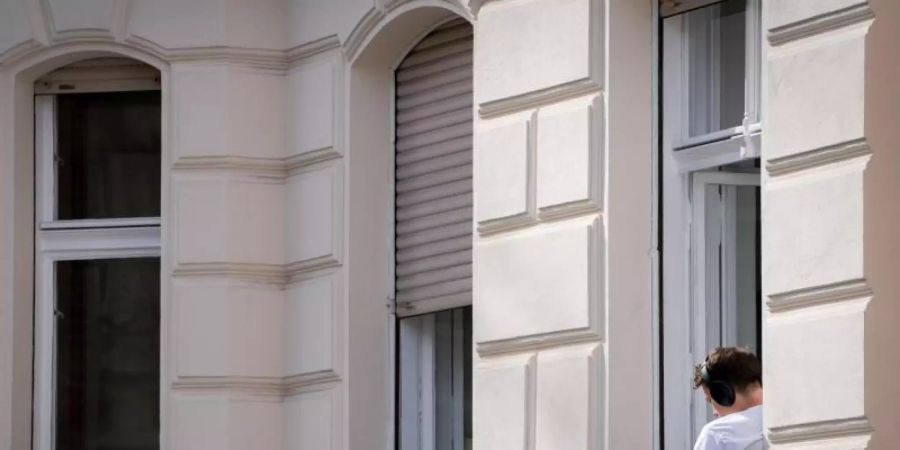 Ein Mann hat sein Homeoffice auf die sonnige Fensterbank seiner Wohnung in Berlin verlegt. Foto: Kay Nietfeld/dpa