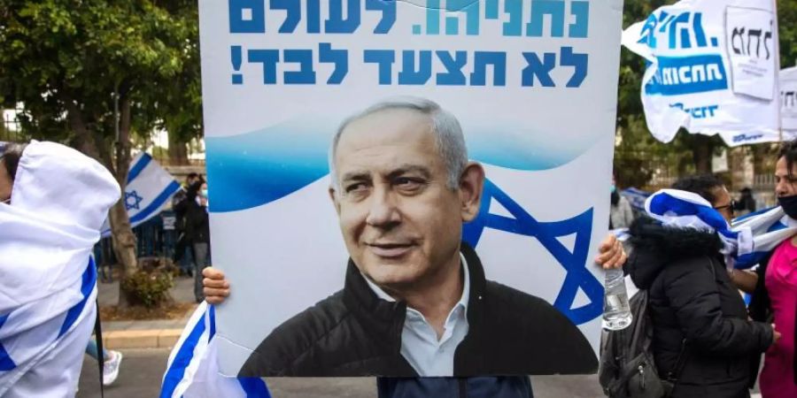Anhänger von Ministerpräsident Netanjahu schwenken Fahnen und halten Plakate vor seiner Residenz in Jerusalem hoch. Foto: Ariel Schalit/AP/dpa