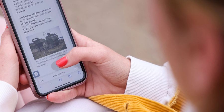 Eine junge Frau liest auf ihrem Smartphone über den Krieg in der Ukraine. Die Krisen der Zeit belasten Jüngere mehr als Ältere.