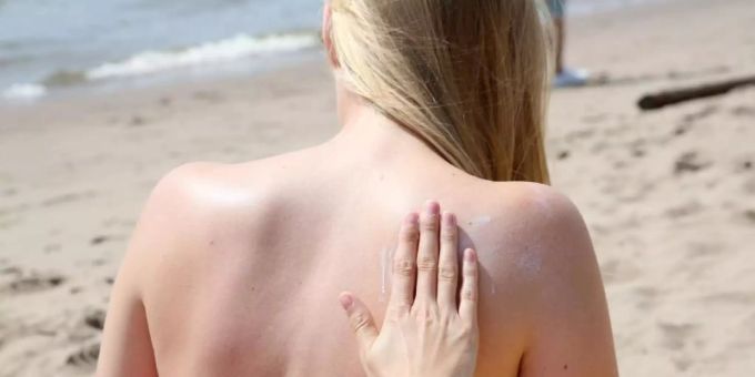 Eine junge Frau wird am Strand mit Sonnencreme eingerieben. Foto: Bodo Marks Sonnenbrand
